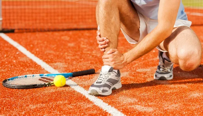 Tennis player holding his ankle after an on-court injury
